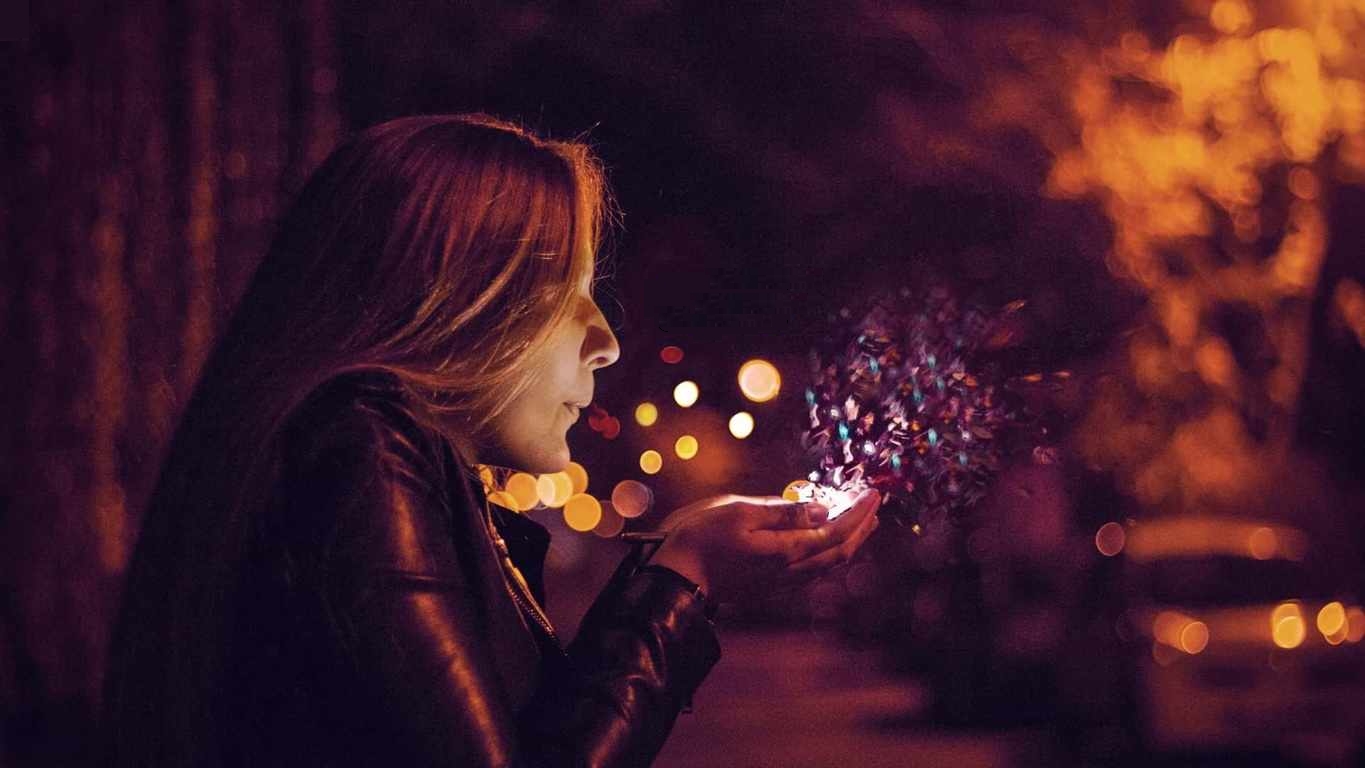 Girl blowing sparkling magic powder from her palms, in the city at night